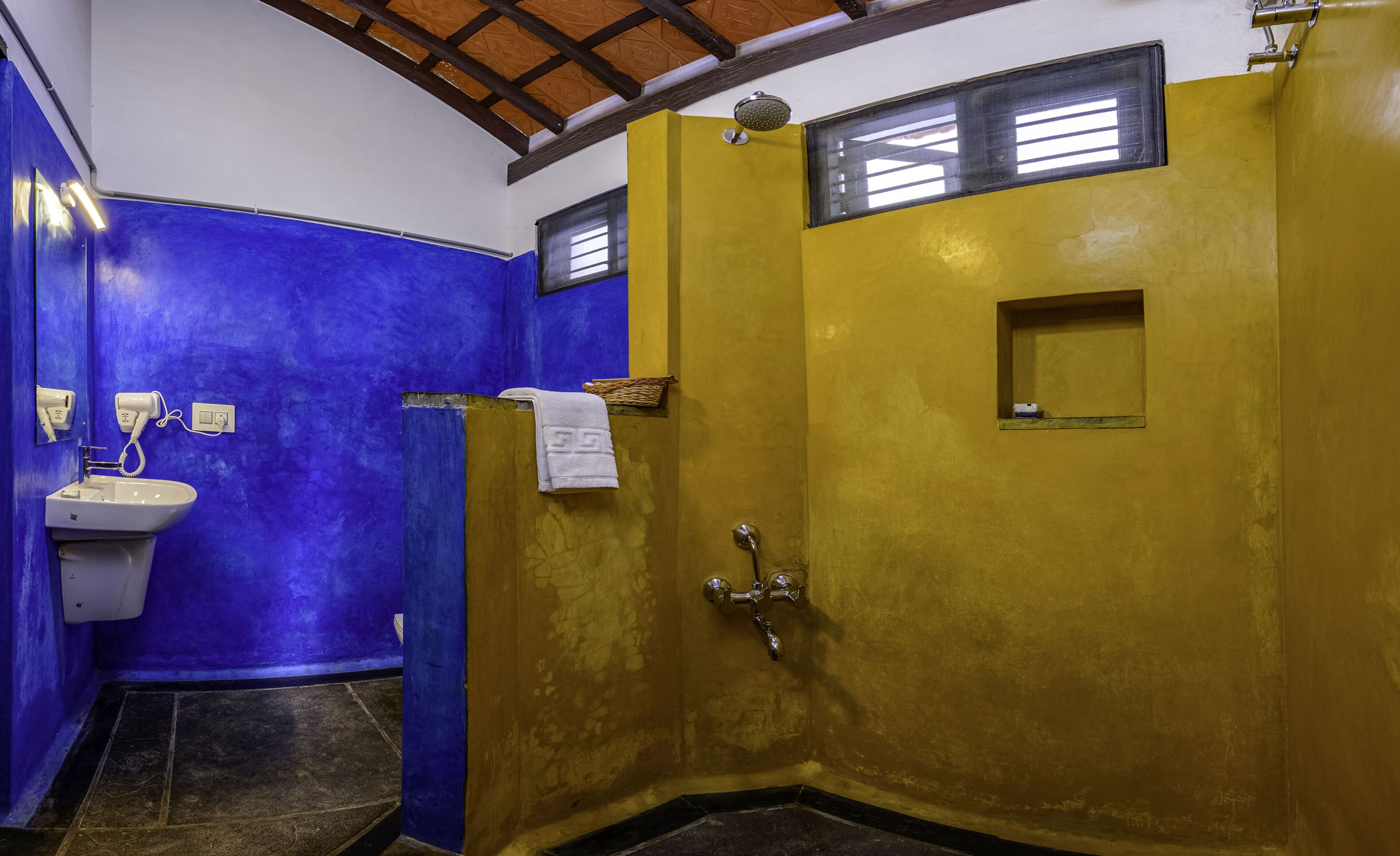 Un baño con una decoración azul y amarilla, un lavamanos con secador de pelo y una ducha con cabezal de ducha manual.