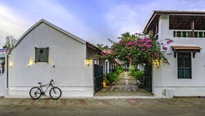 Un edificio blanco con una bicicleta estacionada afuera, una escalera que lleva a una puerta y un balcón con barandas verdes.