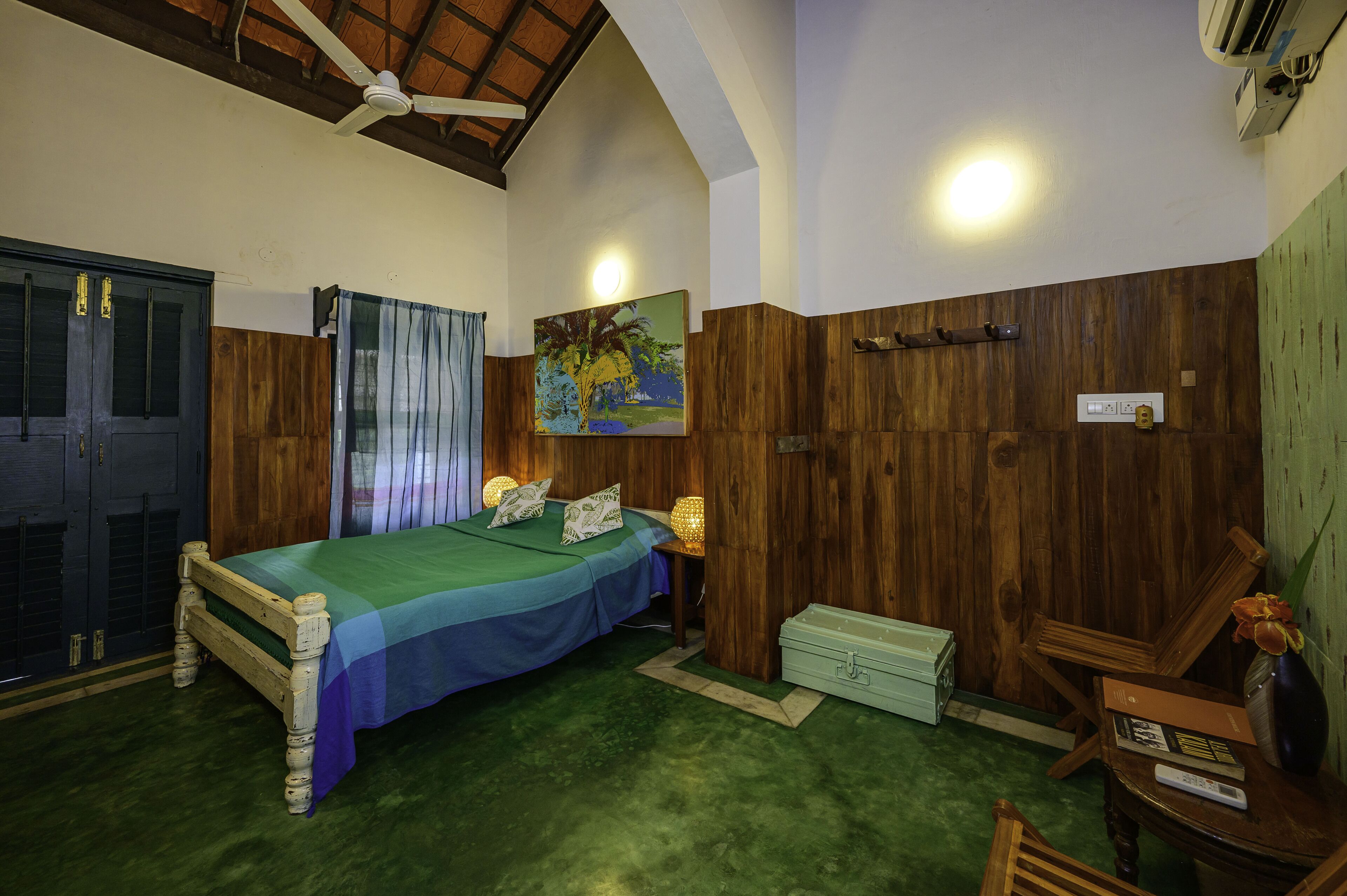 Een slaapkamer met een bed, houten wanden, een plafondventilator, een schilderij en een groen tapijt.
