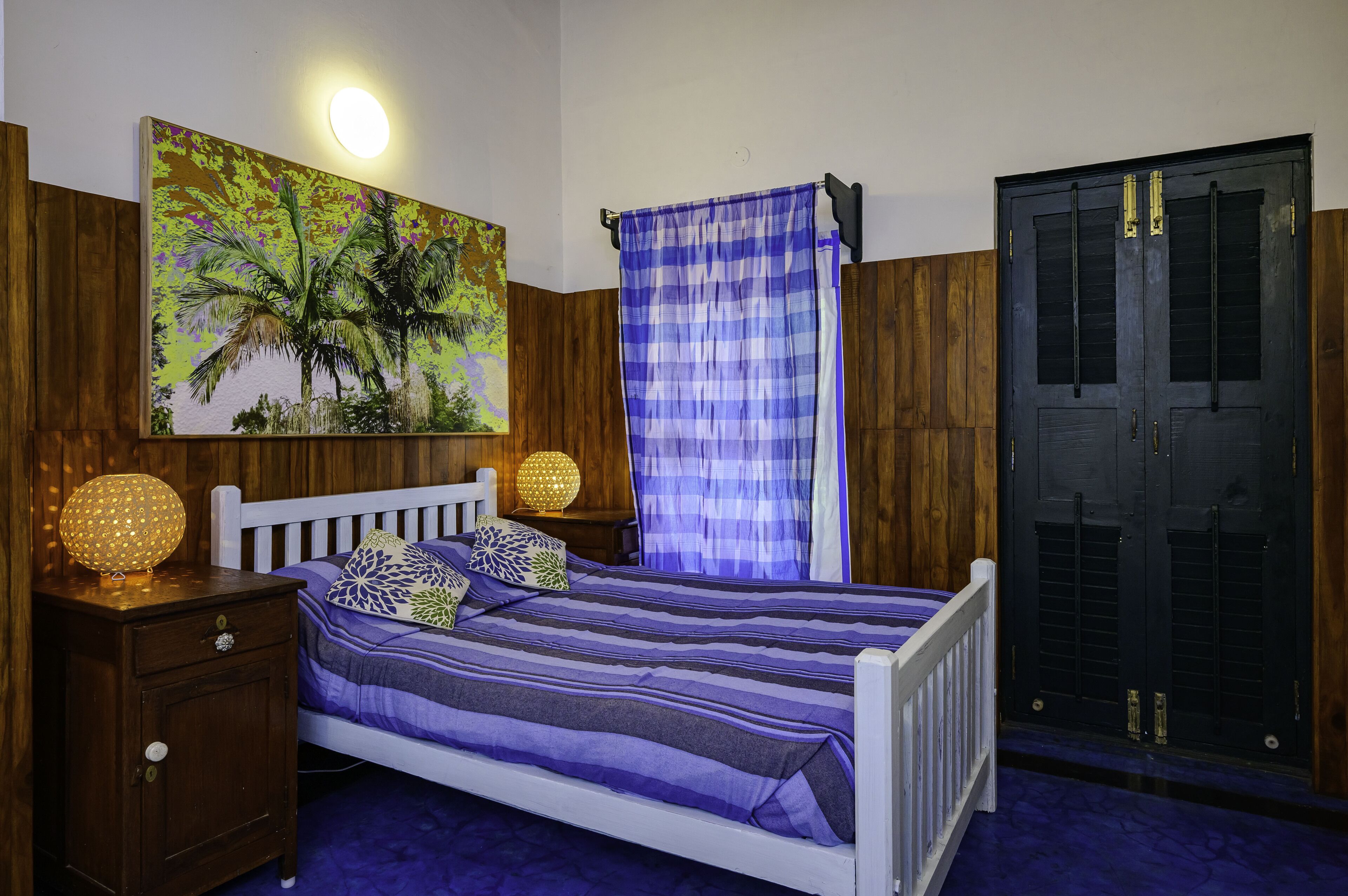 A bedroom with a bed, nightstand, lamp, and a door.