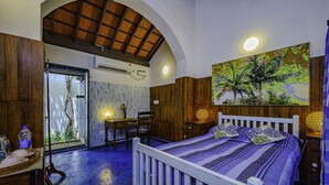 Un dormitorio con cama, escritorio y silla. Se ve una ventana con vista a plantas.