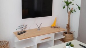 Ett modernt vardagsrum med en platt-TV som är monterad på väggen, ett träbord med lådor, en liten krukväxt och ett vitt bord med dekorativa föremål.