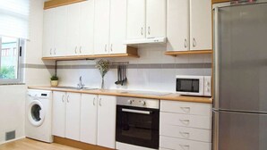 Ett modernt kök med vita skåp, ett kylskåp i rostfritt stål, en mikrovågsugn, en tvättmaskin och en bänkskiva i trä.