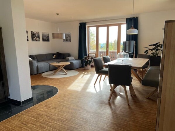 Un salon moderne comprenant un canapé, une table basse ronde, une table à manger avec des chaises et une grande fenêtre avec des rideaux.