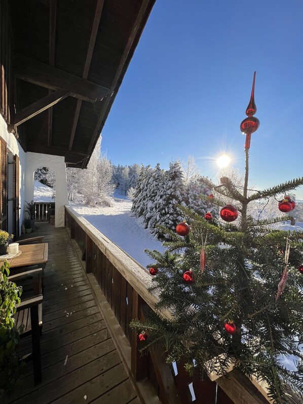 Eine Holzterrasse mit Blick auf eine verschneite Landschaft und einen geschmückten Weihnachtsbaum.