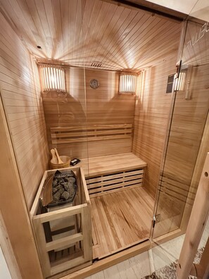 Un sauna avec des murs et des bancs en bois, une porte en verre et un banc en bois sur lequel sont posés une serviette et un petit radiateur.