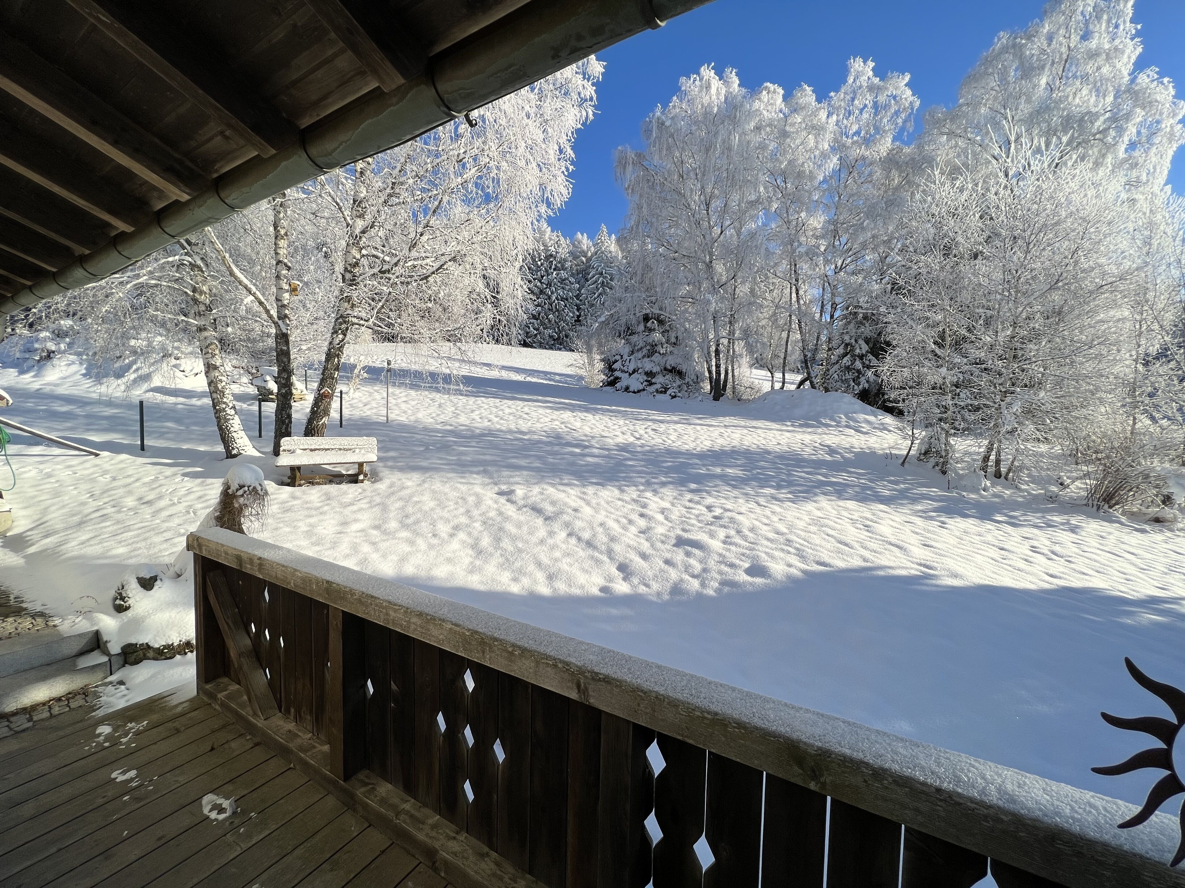 A wooden deck with a snow-covered landscape, including trees and a bench.