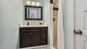 A bathroom with a dark wooden vanity, a mirror, and a shower area with a tiled floor. - Vintage Frenchmen Hideaway,6Blocks to Quarter+Jazz (New Orleans)