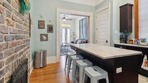 A kitchen with a brick wall, a large island with stools, and a dining area with a couch and table. - Vintage Frenchmen Hideaway,6Blocks to Quarter+Jazz (New Orleans)