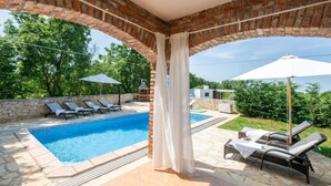 Ein Poolbereich mit Backsteinbogen, Liegestühlen und Sonnenschirmen.