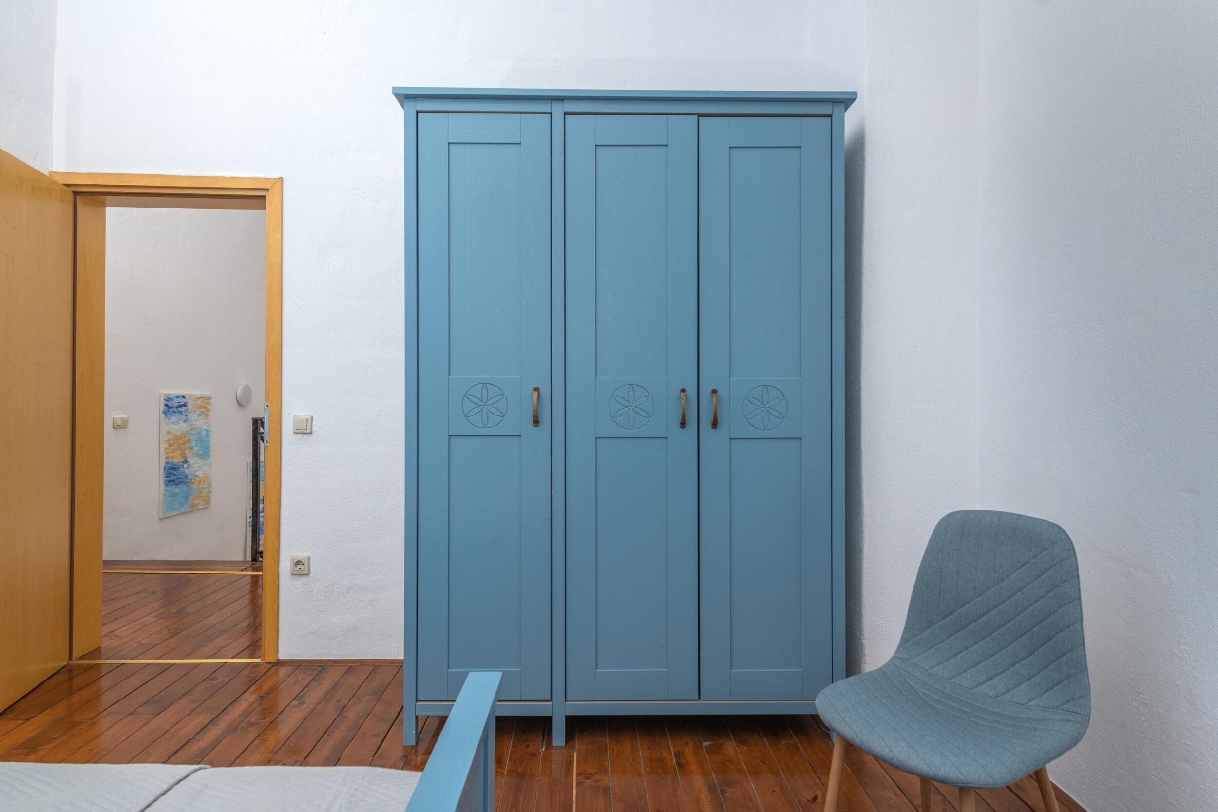 Ein Zimmer mit einem blauen Kleiderschrank, Holzboden und einem grauen Sessel.