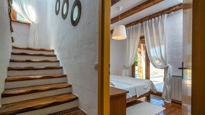Eine Holztreppe führt zu einem Schlafzimmer mit einem Bett, einem Fenster mit Vorhängen und einer Hängelampe.