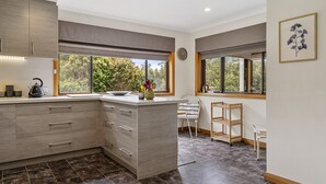 A modern kitchen with a central island, large windows, and a view of trees. - Lumeah Retreat Bruny Island (Adventure Bay)
