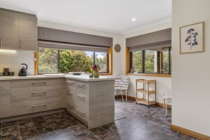 Una cocina moderna con una isla central, ventanas amplias y vistas a árboles.