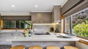 A modern kitchen with a large island, bar stools, and a view of a garden. - Lumeah Retreat Bruny Island (Adventure Bay)