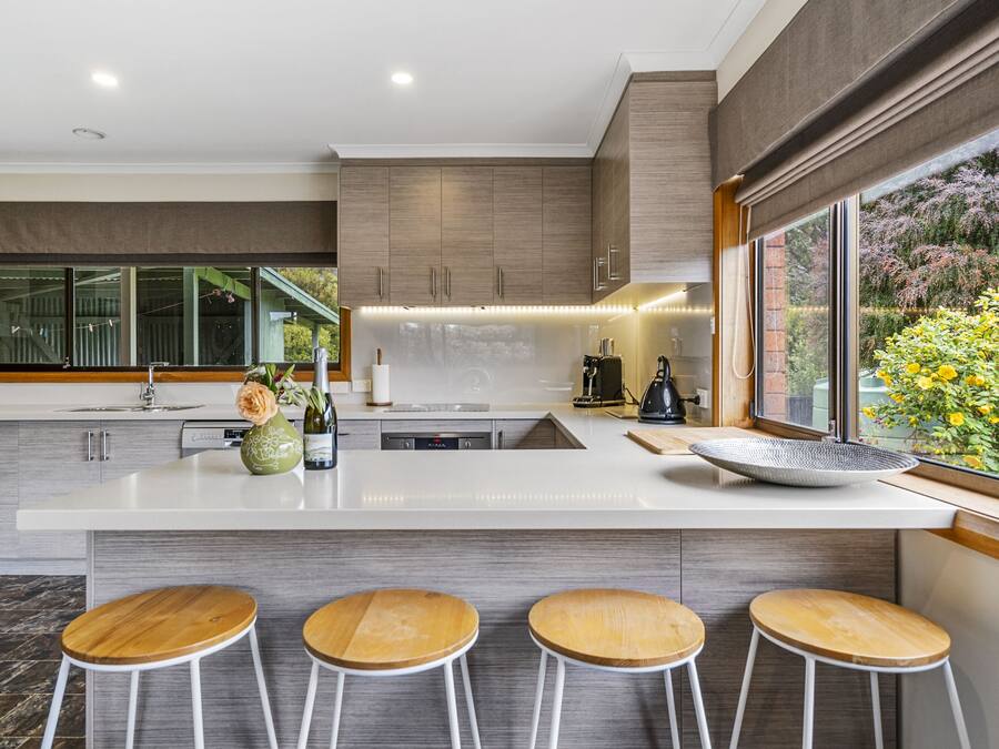 A modern kitchen with a large island, bar stools, and a view of a garden.