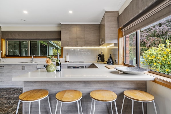 A modern kitchen with a large island, bar stools, and a view of a garden.