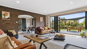 A spacious living area with a leather sofa, a coffee table, and a dining table. There is a large window providing a view of the garden. - Lumeah Retreat Bruny Island (Adventure Bay)