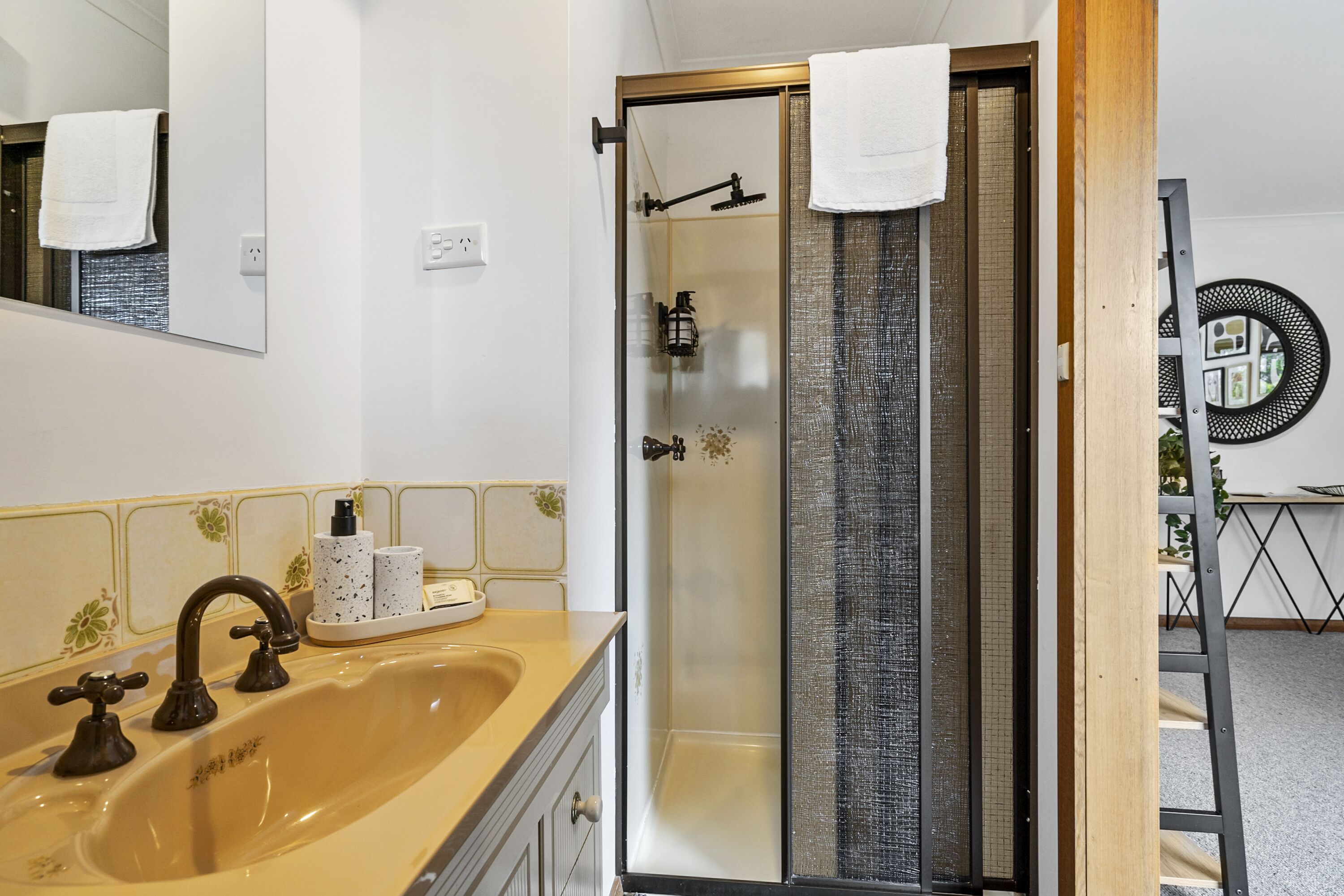A bathroom with a beige sink, a glass-enclosed shower, and a mirror with a towel hanging on it.