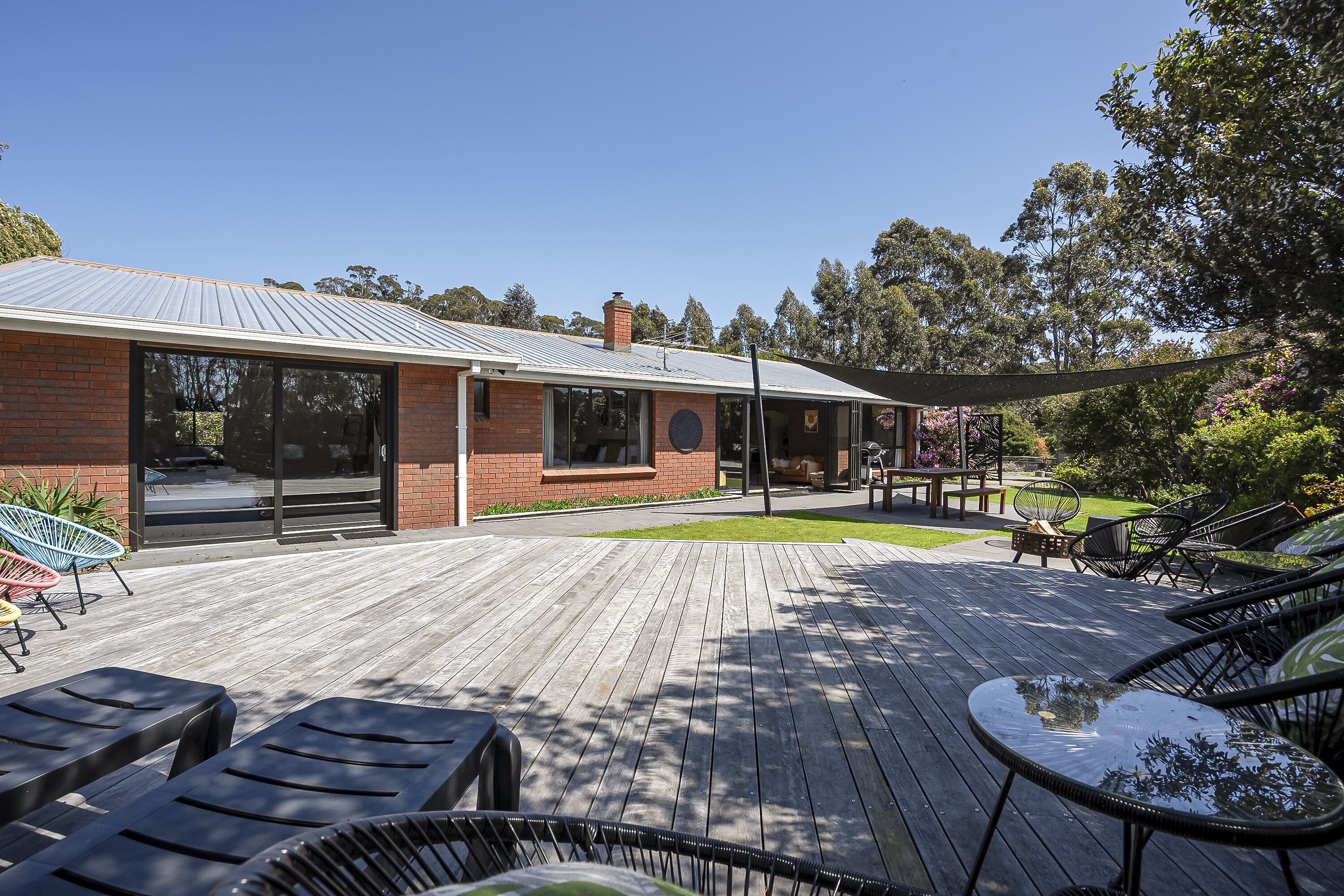 Une terrasse en bois avec des meubles d’extérieur, un bâtiment en briques doté de grandes fenêtres et une pelouse.