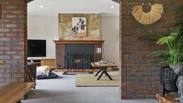 Ein Wohnzimmer mit Kamin aus Backsteinen, einem Fernseher und einer Couch.