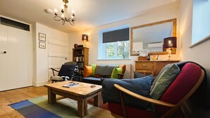 A cozy living room with a wooden coffee table, a sofa with colorful cushions, a bookshelf, and a large mirror above a dresser.