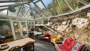 A conservatory with a stone wall, wooden furniture, and a glass ceiling.