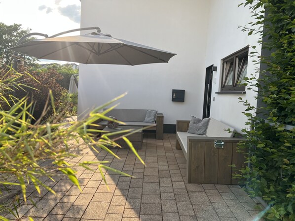 Un espace patio avec un banc en bois, une table et un parasol.
