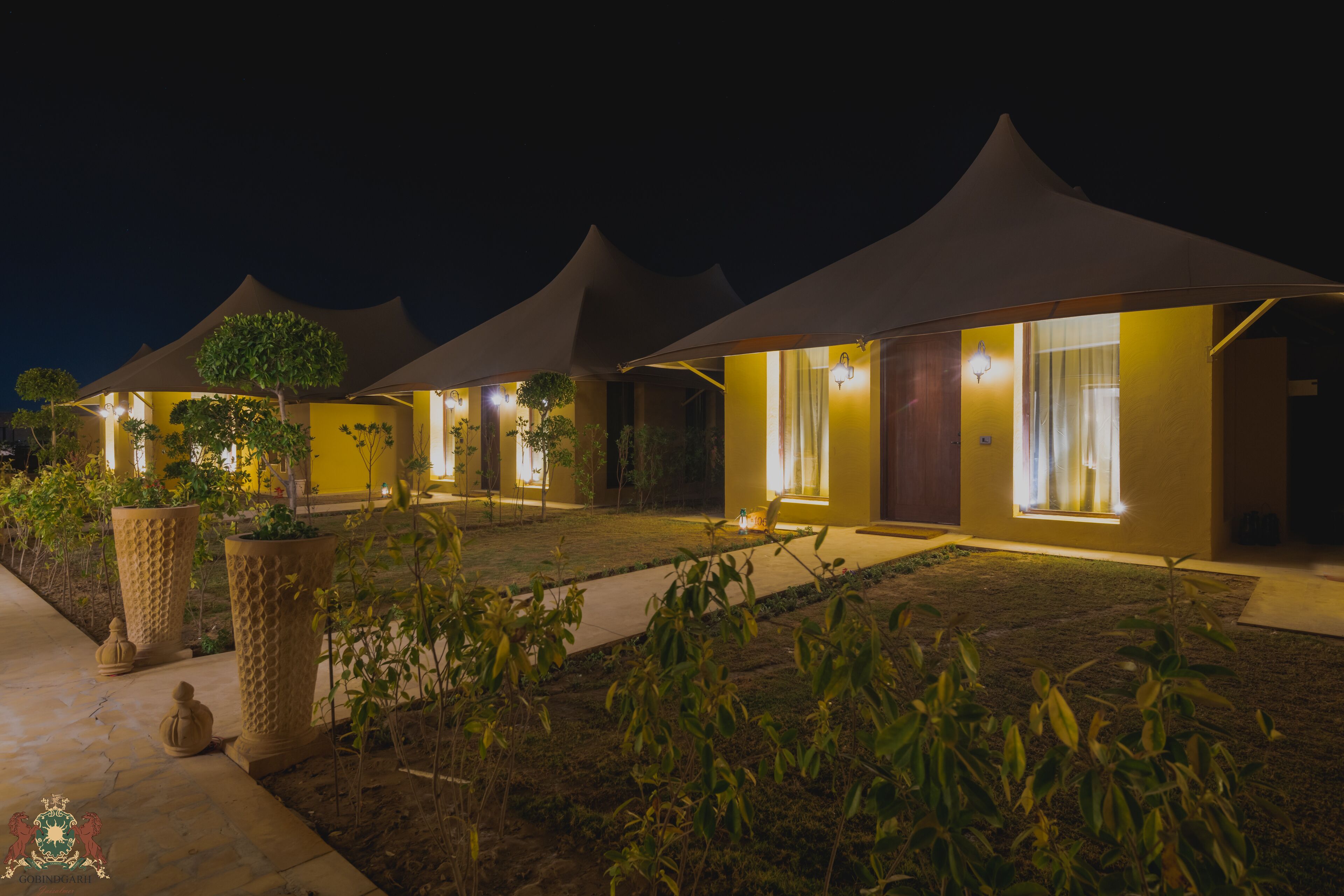A row of modern, well-lit villas with large windows and a garden area in the foreground.