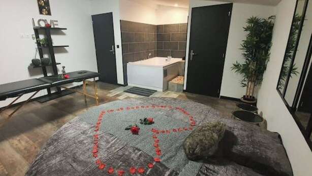 Et værelse med en bænk, et lille bord, en potteplante og et hjerteformet arrangement af røde roser på gulvet.