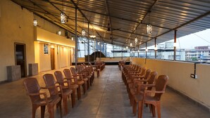 A spacious indoor area with rows of wooden chairs and tables, large windows, and a high ceiling with metal beams. - Hotel Golden suites Vashi Navi mumbai  (Navi Mumbai)