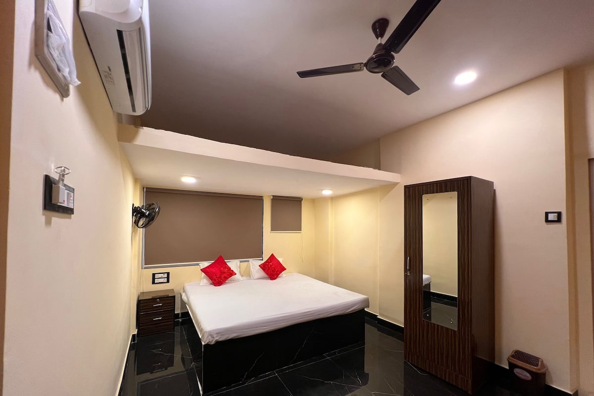 A hotel room with a bed, a ceiling fan, an air conditioning unit, a mirror, and a small trash bin.