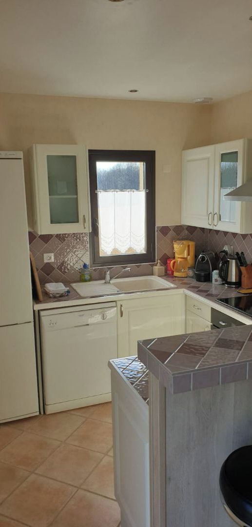 Une cuisine de taille réduite avec des meubles blancs, une fenêtre, un lave-vaisselle et un pare-feu en carrelage.