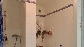 Une salle de bain avec une douche, un lavabo et un miroir. On y trouve un porte-serviettes et une étagère avec des articles de toilette.