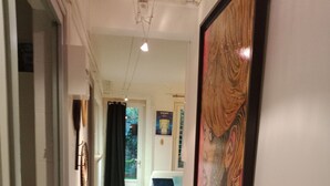 Un couloir au sol en bois, un lit avec une literie blanche et un tableau encadré accroché au mur.