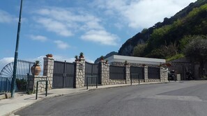 Ein verschlossenes Tor mit einer Steinmauer und Metallgittern, eine gepflasterte Straße und eine gebirgige Kulisse.