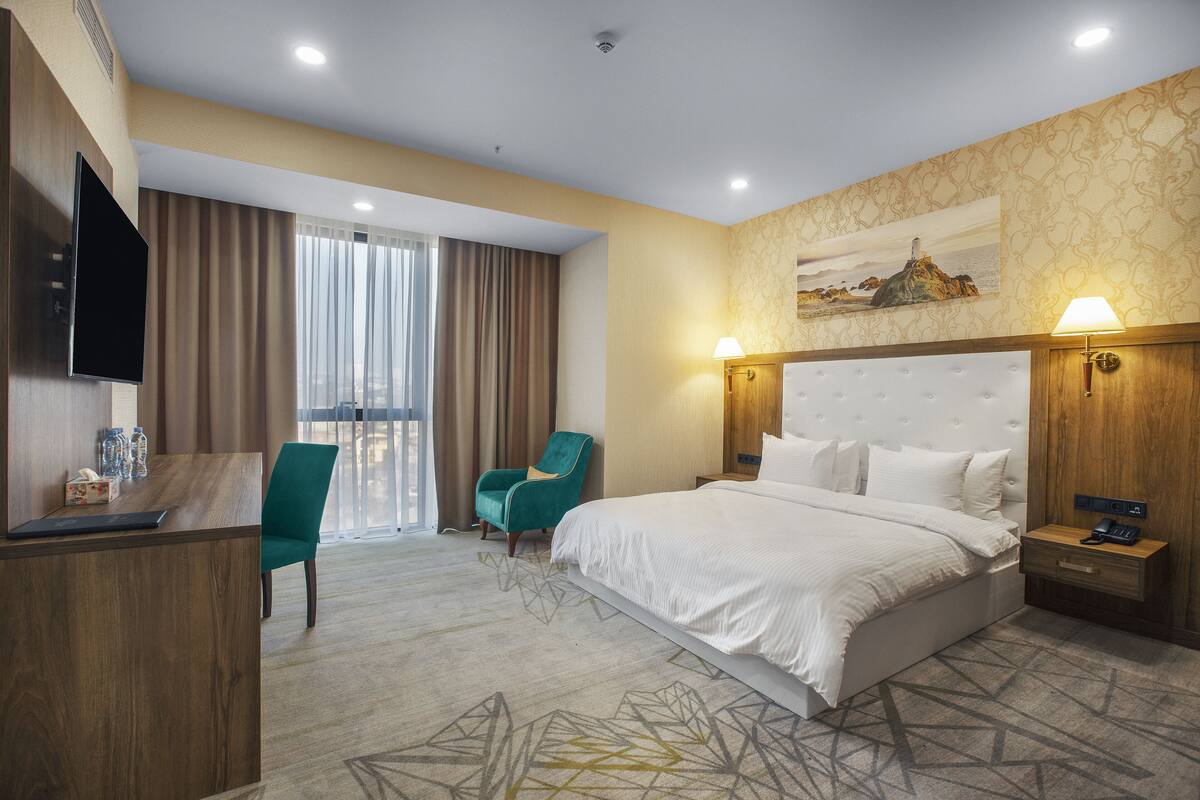 A hotel room with a bed, a desk, a chair, a TV, and a painting on the wall.