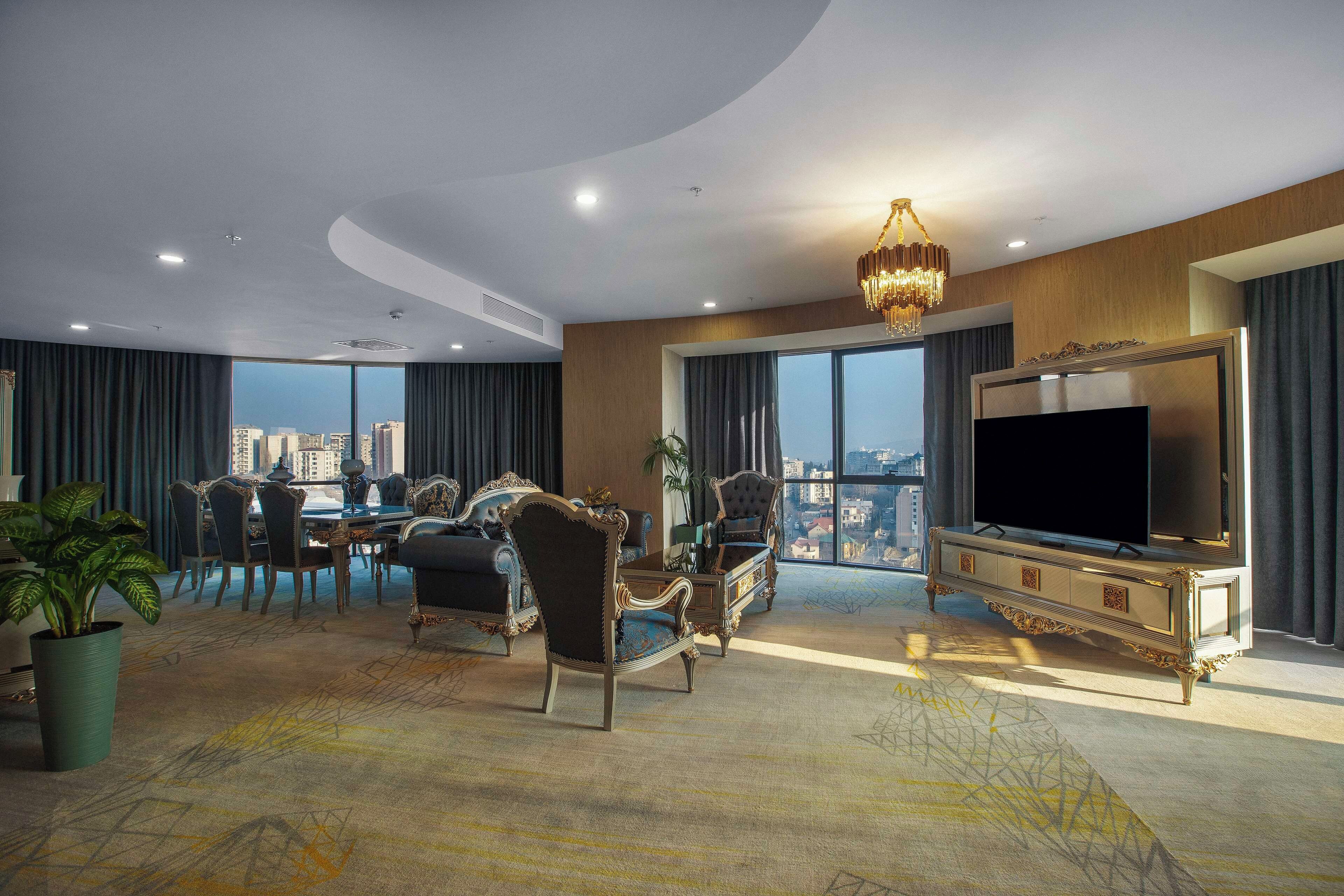 A spacious living room with a large TV, elegant furniture, and a city view.
