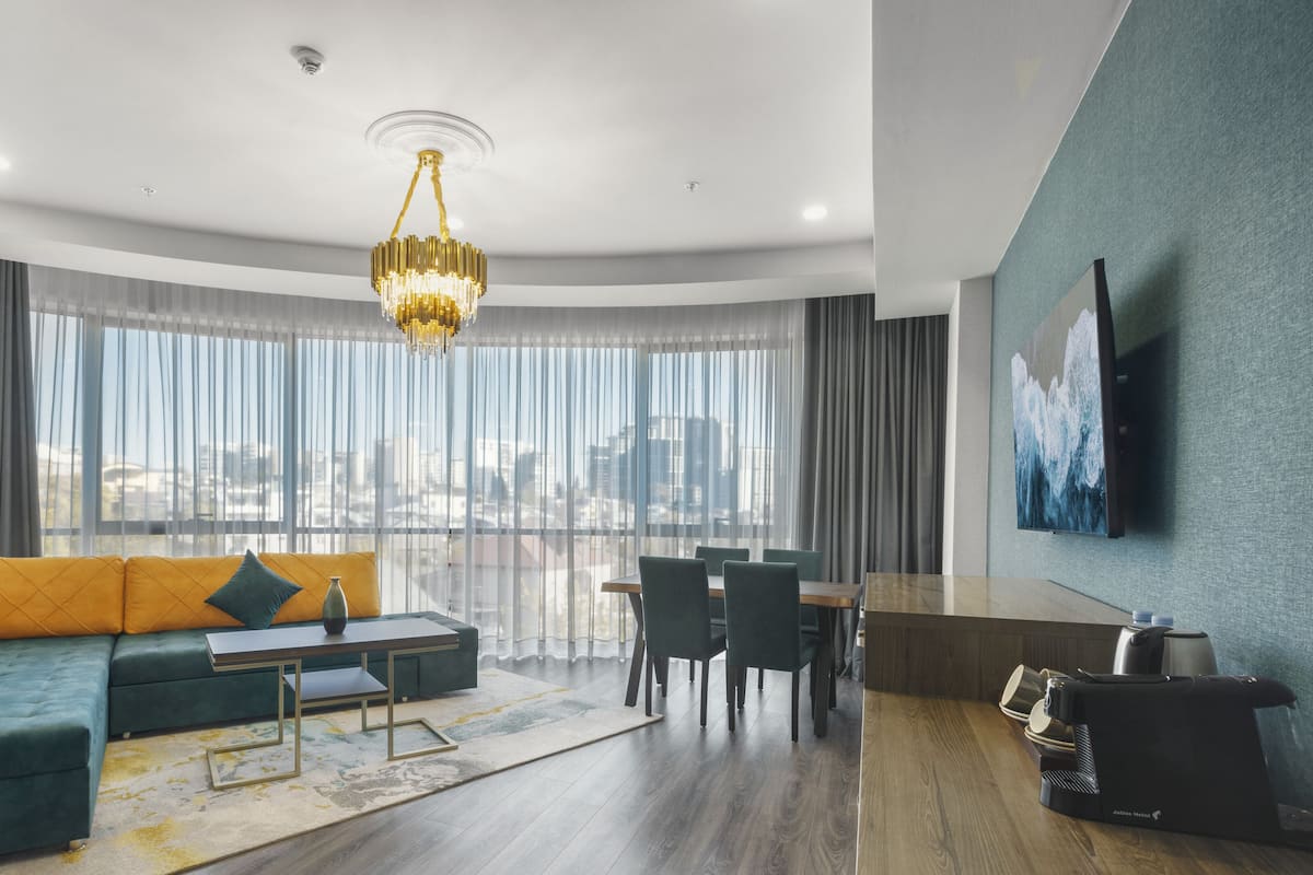 A modern living room with a green sofa, a dining area, and a city view through large windows.