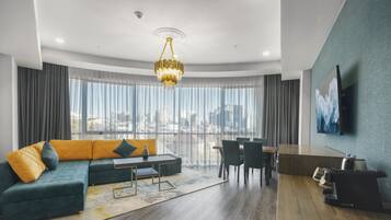 A modern living room with a green sofa, a dining area, and a city view through large windows.