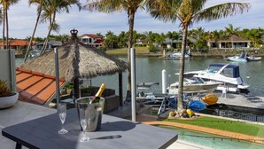 A view of a marina with boats docked, a thatched-roof structure, and a table with a champagne bottle and glasses. - Paradise on Banksia Canal (BANKSIA BEACH)