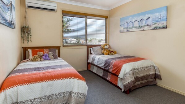 A bedroom with two beds, a window with blinds, an air conditioner, and wall art.