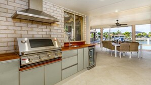 A kitchen with a stainless steel range, a brick wall, and a dining area with a view of the water. - Paradise on Banksia Canal (BANKSIA BEACH)