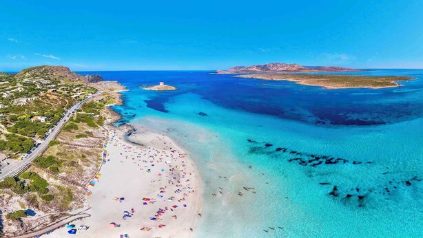 An aerial view of a coastal area with a beach, clear blue waters, and a road leading to a settlement. - Holiday home mit Klimaanlage (Stintino)