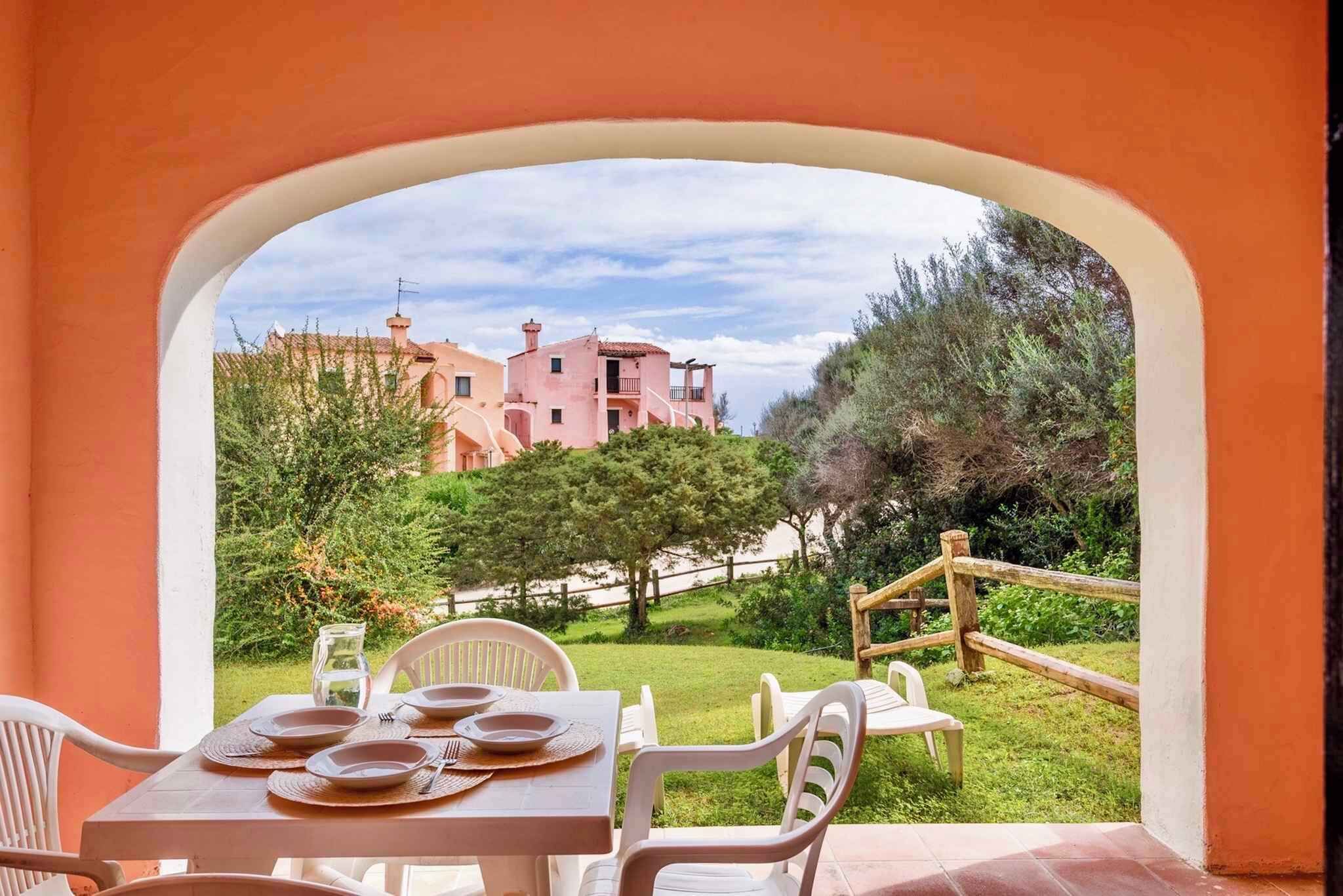 A dining area with a table set for four, overlooking a pink building and a garden.