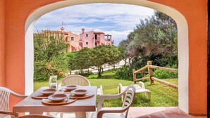 A dining area with a table set for four, overlooking a pink building and a garden. - Holiday home mit Klimaanlage (Stintino)
