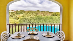 A balcony with a table set for four, overlooking a swimming pool and a lush landscape. - Holiday home mit Klimaanlage und Pool (Stintino)