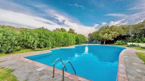 A rectangular swimming pool with a stone border, surrounded by a stone patio and lush greenery. - Holiday home mit Klimaanlage und Pool (Stintino)