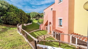 A building with a pink facade, a wooden fence, and a well-maintained lawn. - Holiday home mit Klimaanlage und Pool (Stintino)