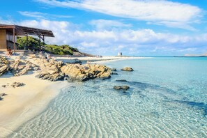 Una playa con aguas cristalinas, costa rocosa y un edificio con zona cubierta.
